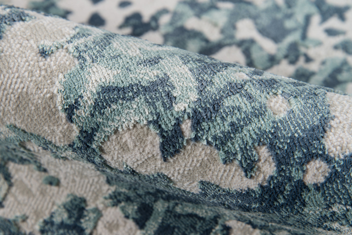 Blue, teal and ivory patterned rug with plush pile; close-up of folded rug.