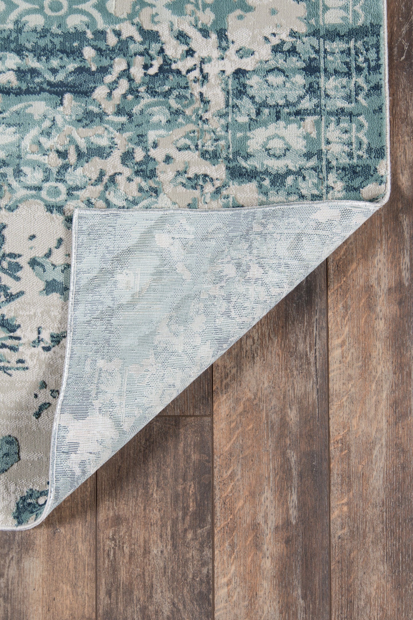 Blue & teal distressed floral runner rug with light backing, folded corner on wood floor.