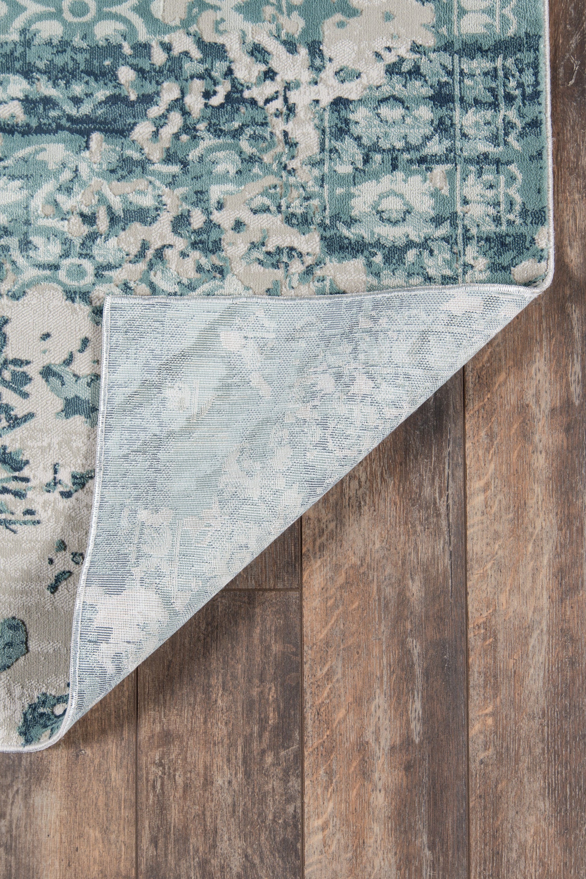 Blue & teal distressed floral runner rug with light backing, folded corner on wood floor.