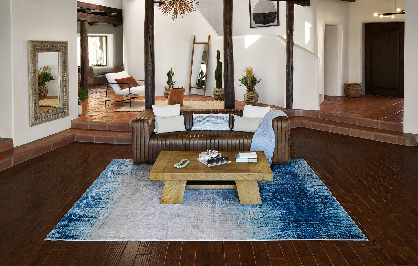 Living room with brown leather sofa, blue gradient rug, wooden coffee table & exposed beams.
