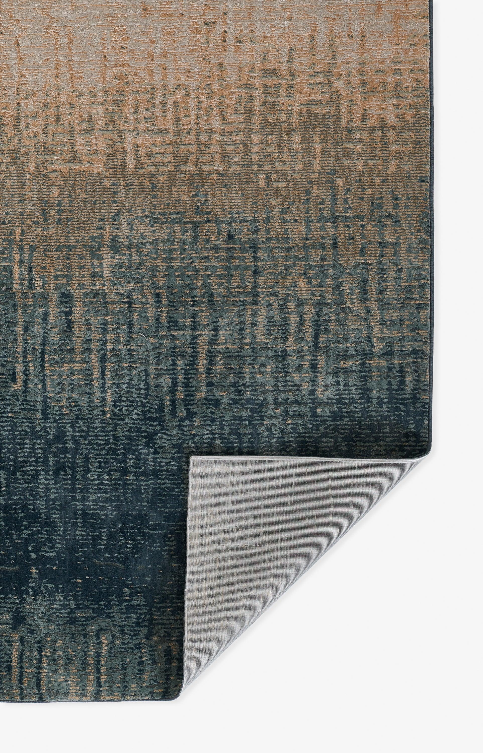 Gradient blue-to-brown woven area rug with textured vertical pattern; modern rectangular, folded corner reveals underside.