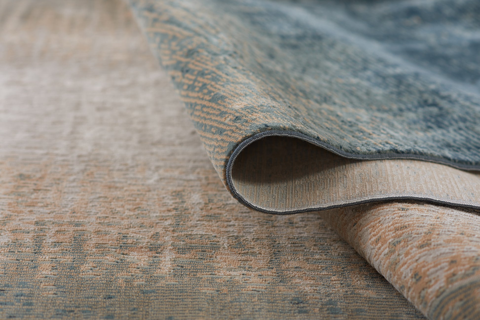 Blue and beige woven rug with a textured pattern, rolled edge showing layered weave; warm home decor.