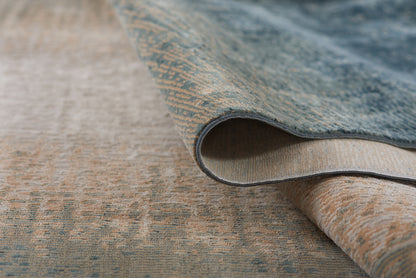 Blue and beige woven rug with a textured pattern, rolled edge showing layered weave; warm home decor.