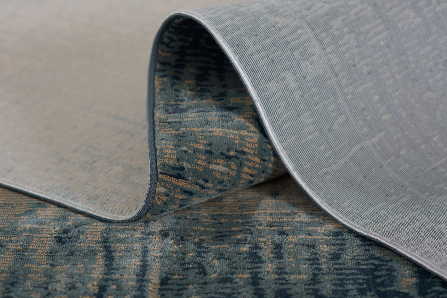 Light gray textured area rug with a rolled edge, exposing a blue patterned underside.