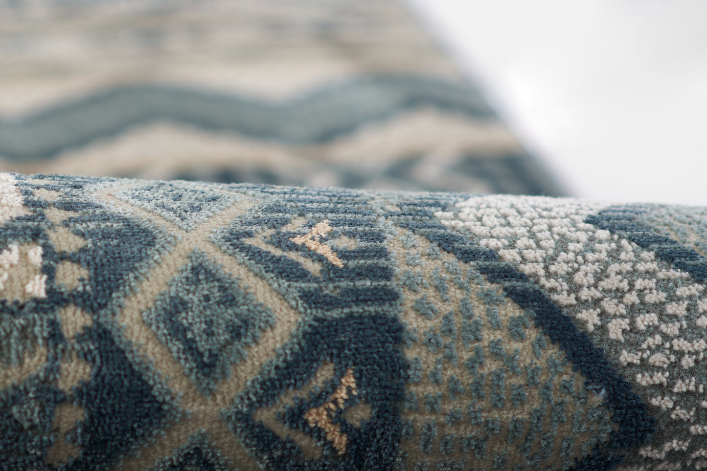 Close-up of a blue woven rug with beige geometric motifs, diamonds and chevrons in a textured pile.