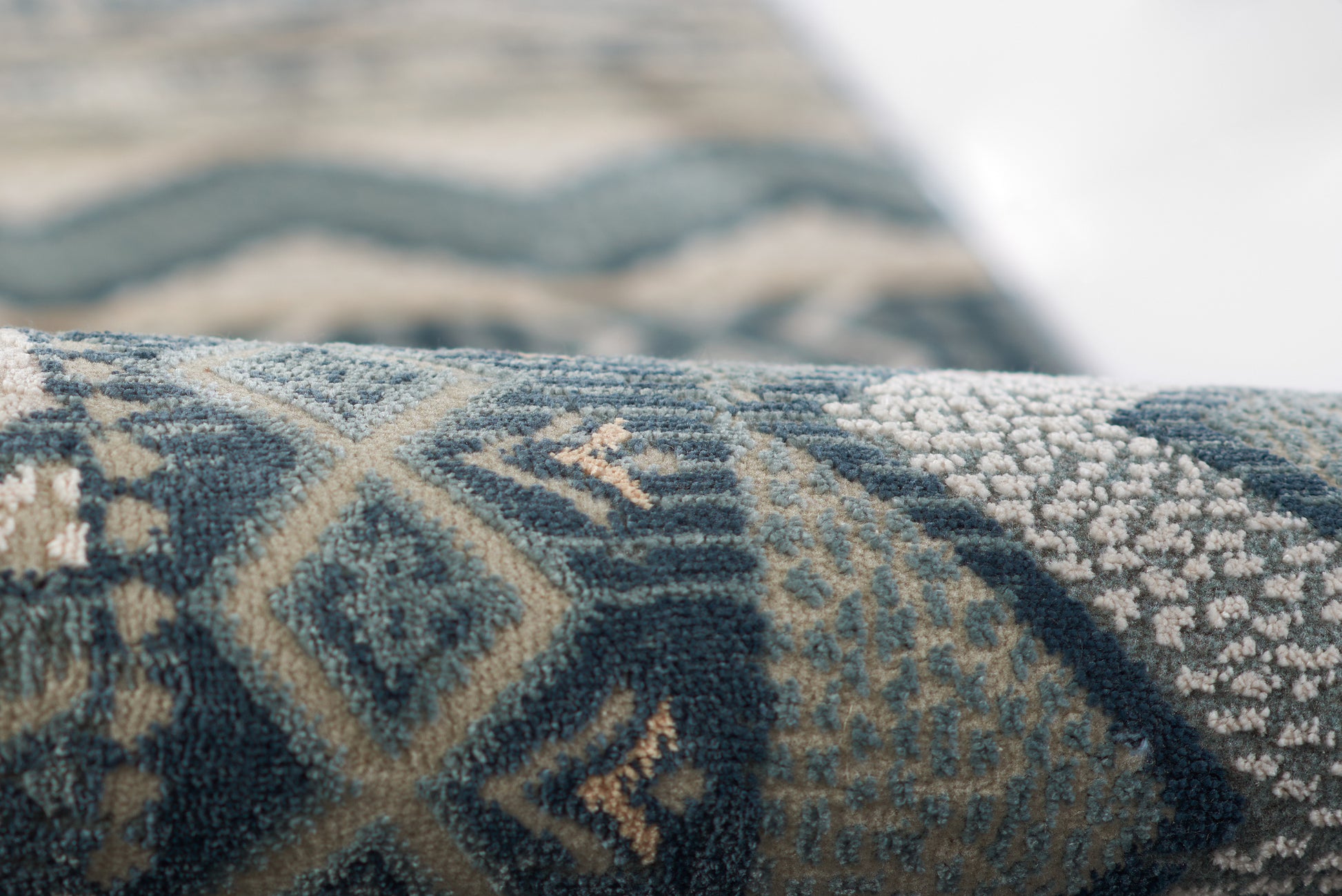Close-up of a blue woven rug with beige geometric motifs, diamonds and chevrons in a textured pile.