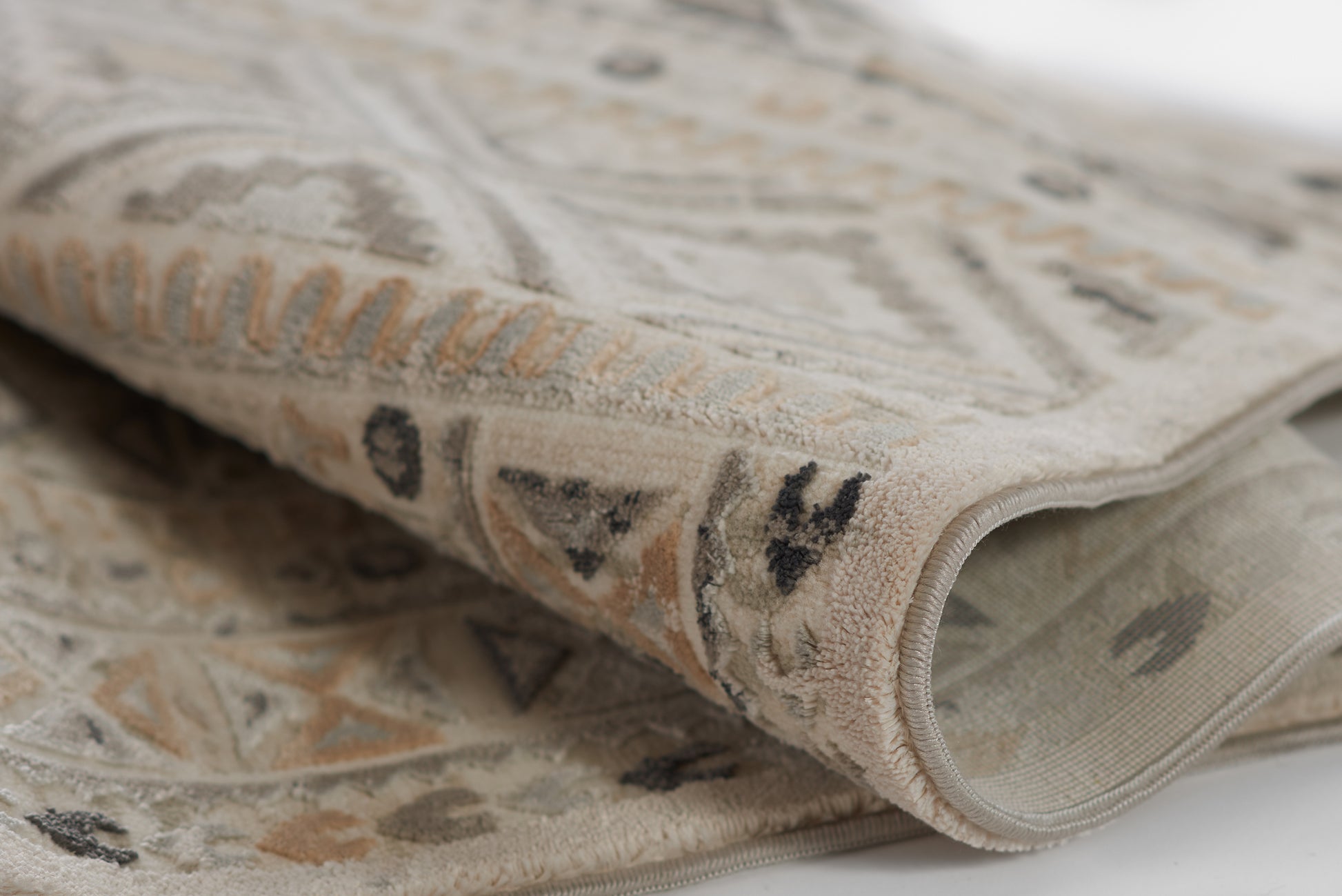 Beige geometric area rug with ivory, gray and tan motifs; soft pile and rolled edge.