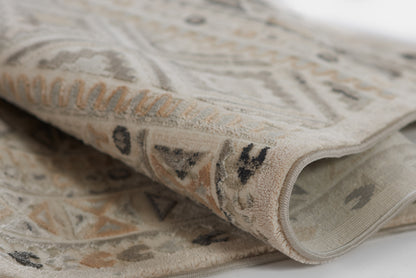 Beige geometric area rug with ivory, gray and tan motifs; soft pile and rolled edge.
