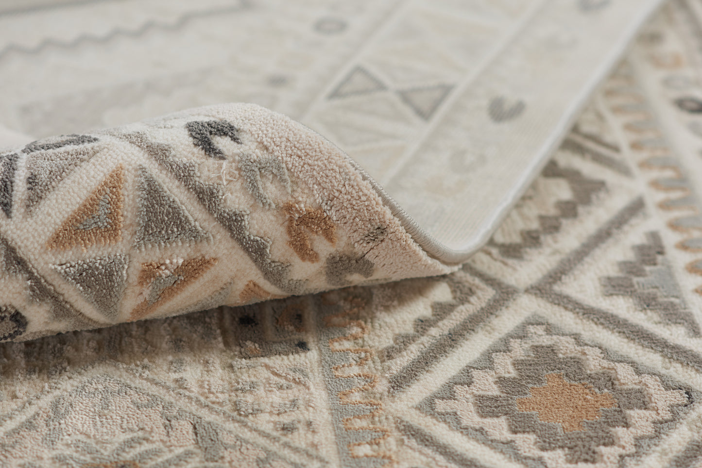 Geometric woven area rug in ivory, gray & taupe with diamonds & triangles; folded corner reveals soft pile.