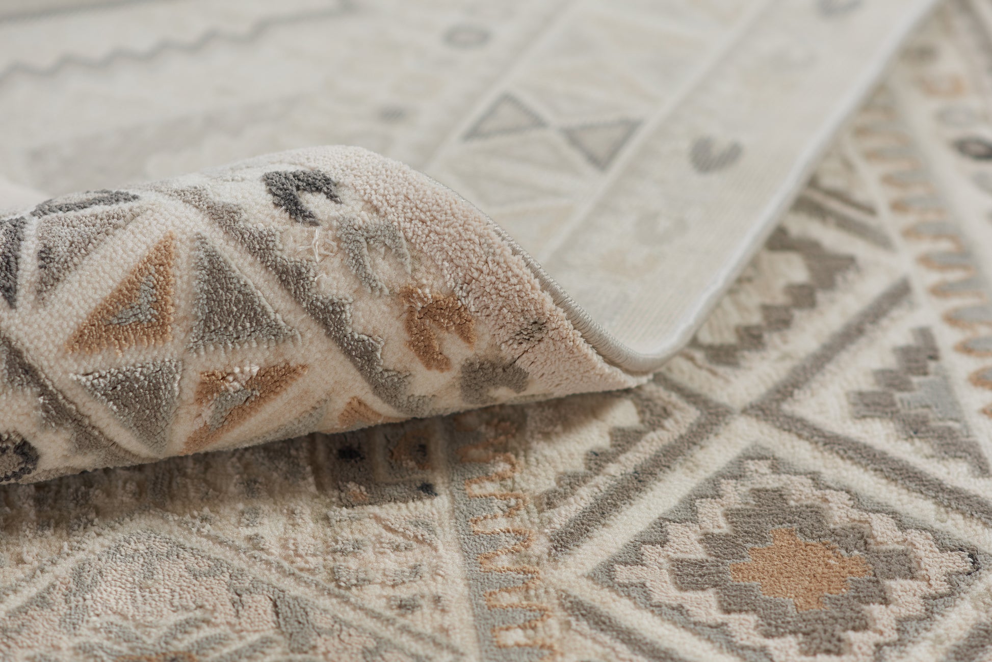 Geometric woven area rug in ivory, gray & taupe with diamonds & triangles; folded corner reveals soft pile.