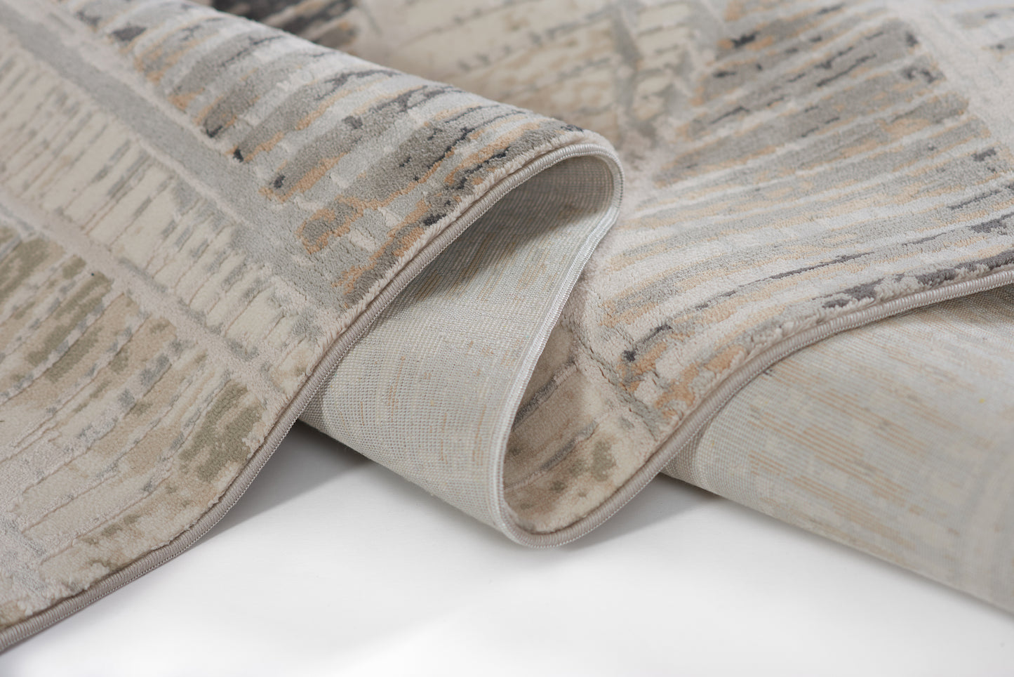 Gray and beige abstract-pattern area rug with soft plush pile; rolled edge reveals light backing.
