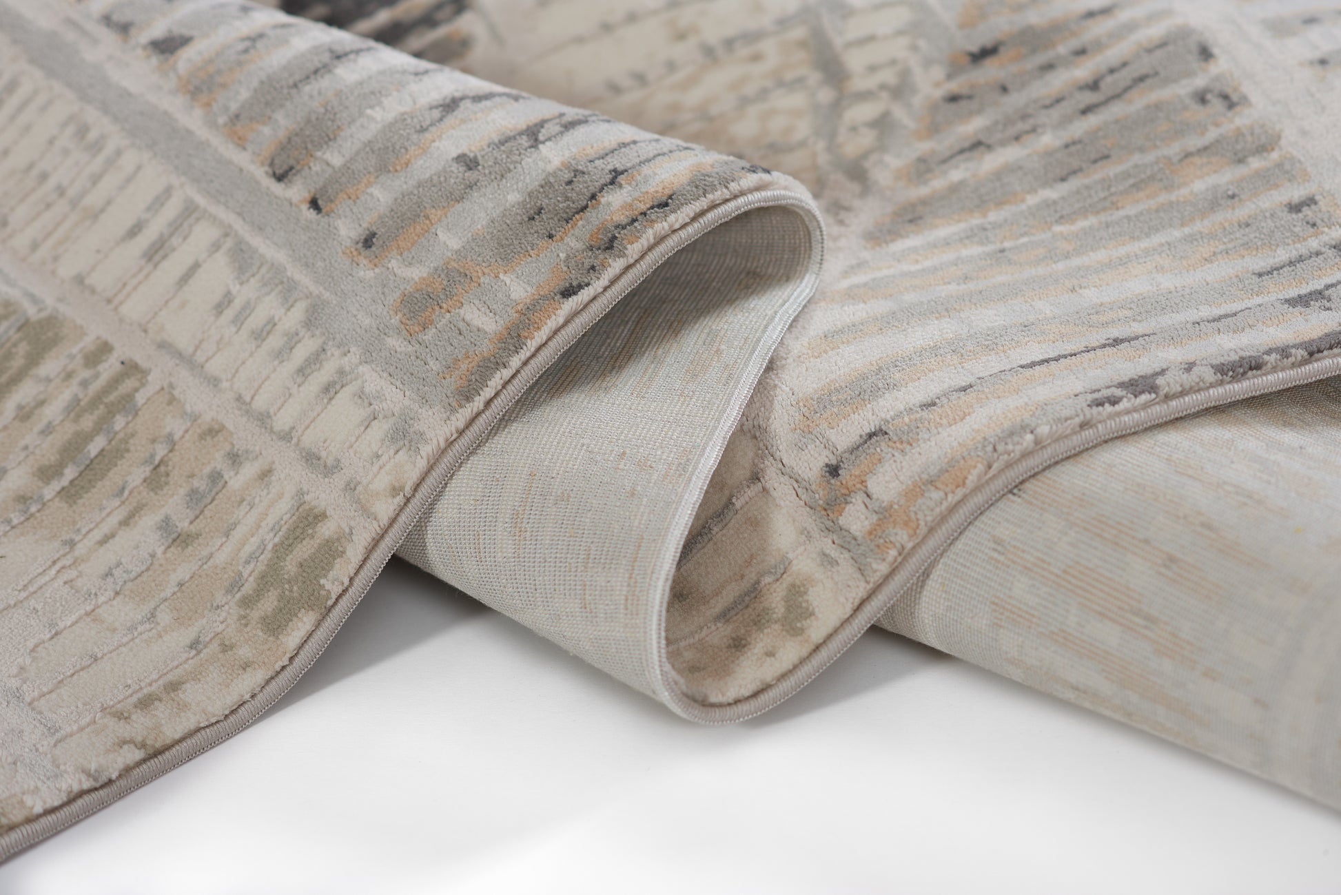 Gray and beige abstract-pattern area rug with soft plush pile; rolled edge reveals light backing.