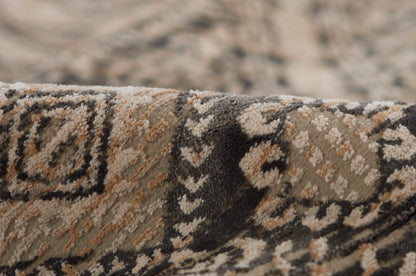 Close-up of a traditional woven rug with beige, brown, black & gray motifs; ornate floor decor.