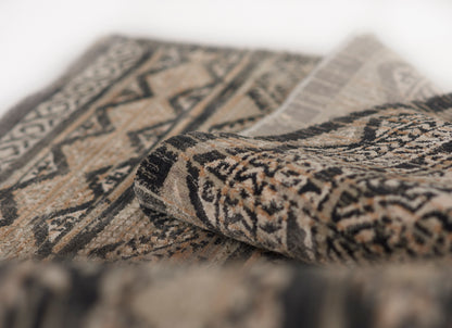 Neutral-toned woven rug with geometric tribal pattern in beige, black and brown, folded to reveal fringe.