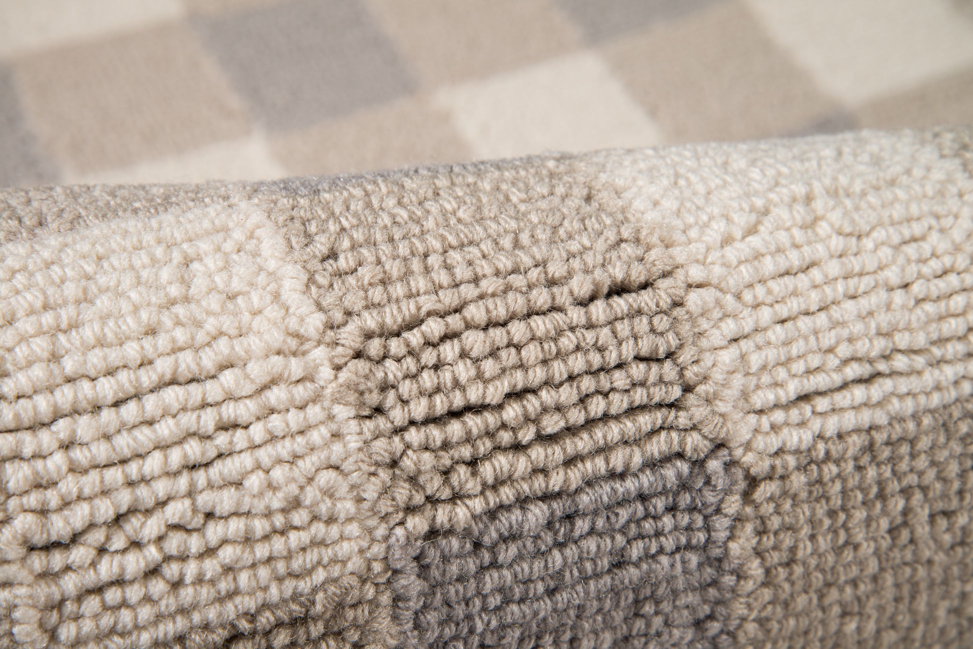Close-up of a thick, looped-pile rug in grey and beige tones with a plush, textured surface.