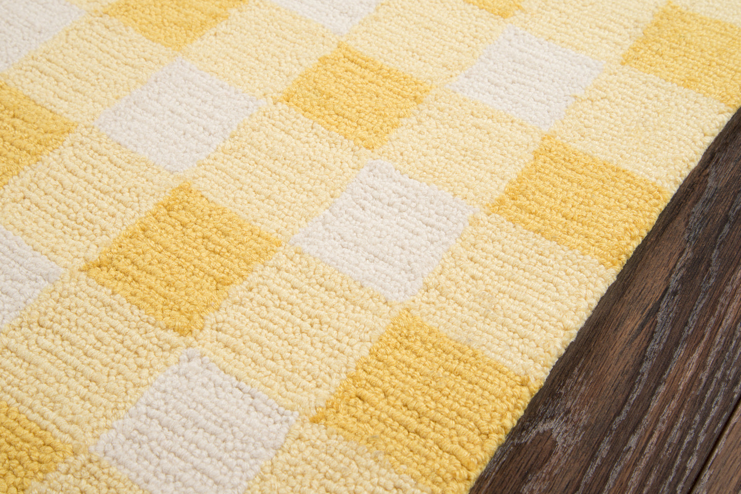 Yellow and white geometric checkered rug with looped texture beside dark wood floor.