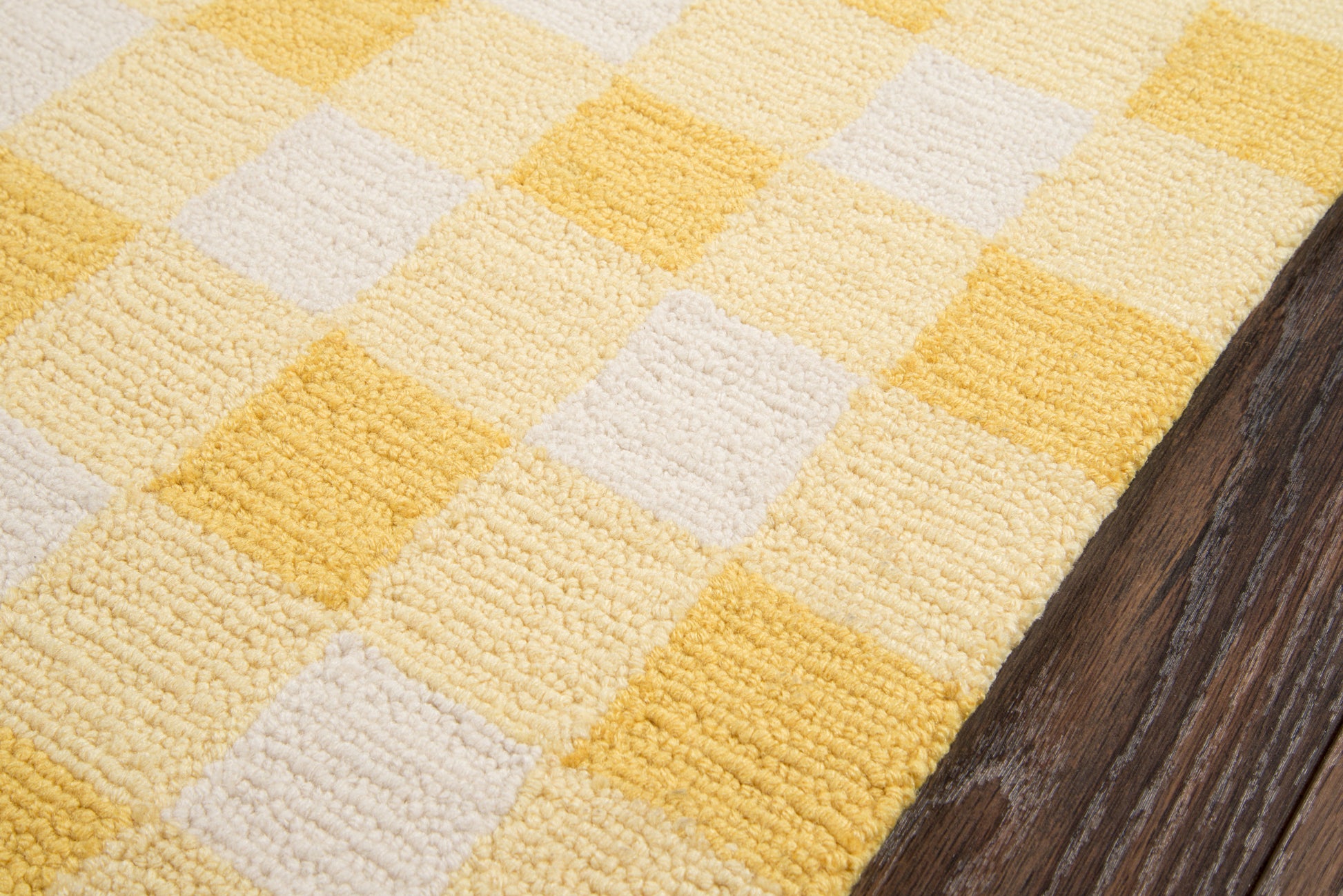 Yellow and white geometric checkered rug with looped texture beside dark wood floor.
