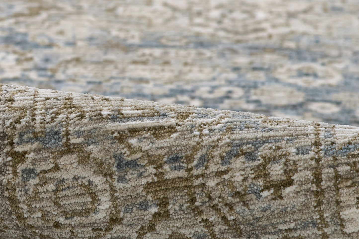 Close-up of beige and blue oriental rug with intricate floral pattern, partially rolled to show texture.