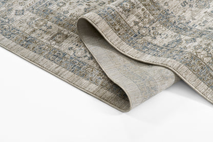 Muted blue-gray Oriental rug with beige distressed pattern; folded edge shows soft backing.