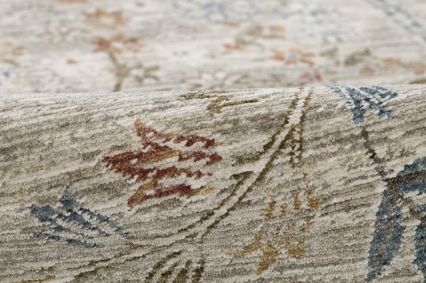 Close-up of a beige, high-pile area rug with multicolored floral vine pattern in red, blue, green and yellow.