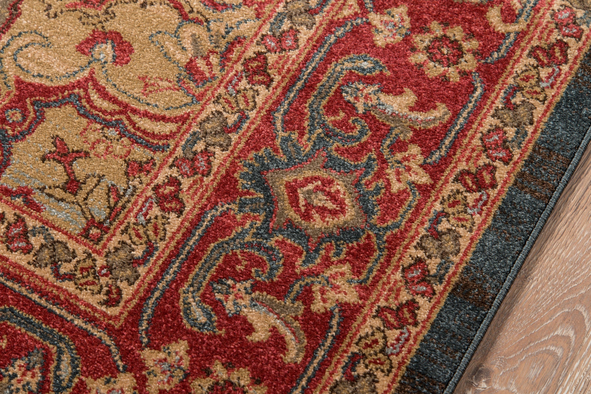 Ornate Persian-style area rug with red, beige, blue and gold motifs and a floral border on a wooden floor.