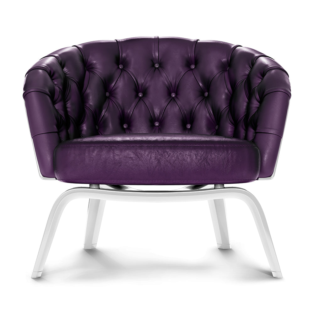 Rich purple tufted leather lounge chair with white metal legs, rounded back & button tufting.