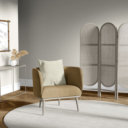 Beige upholstered armchair with pale cushion, light round rug, woven rattan room divider, and slim console table with a vase of dried stems.