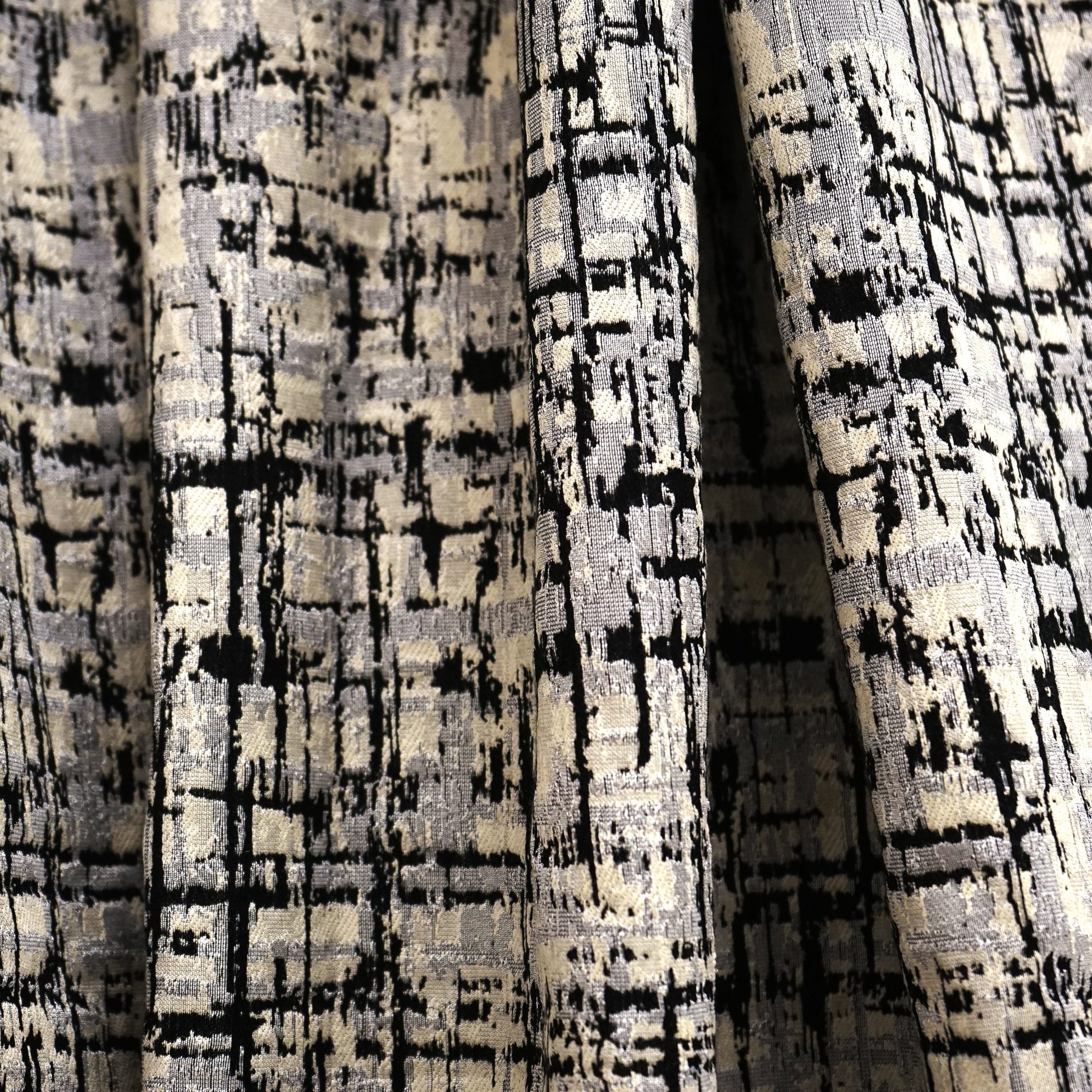 Textured woven fabric with abstract black and cream grid pattern; thick drape, suitable for upholstery or curtains.