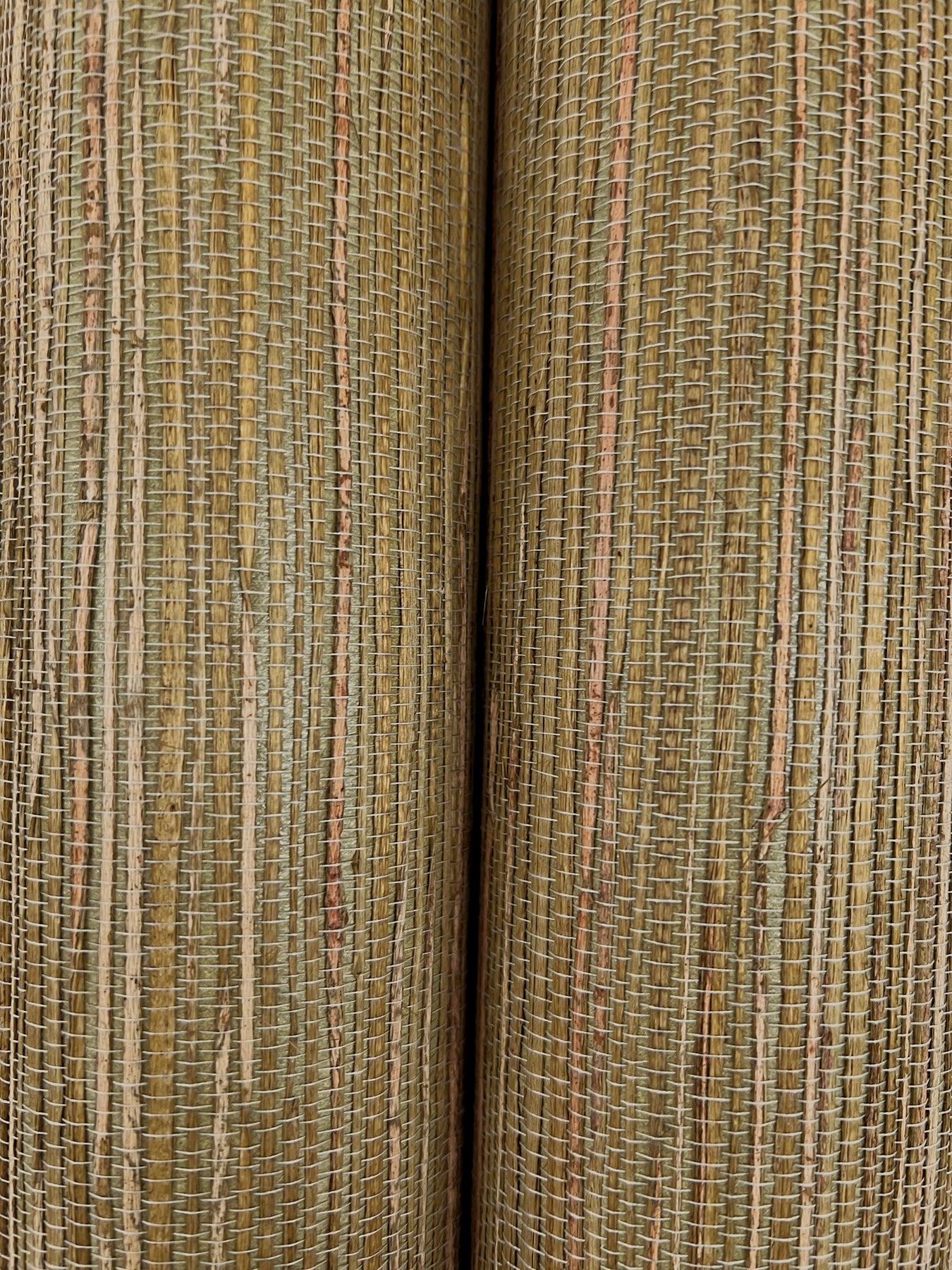 Close-up of two rolled natural woven wallpaper samples with vertical tan and brown stripes.