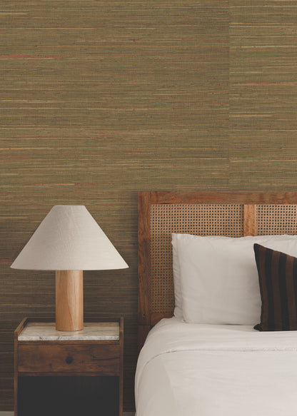 Bedroom wall covered in warm brown grasscloth wallpaper, with a cane headboard, white linens, dark striped pillow, wooden nightstand with marble top, and a lamp.