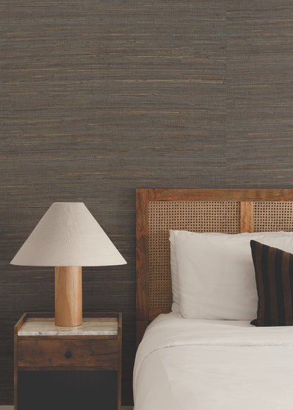 Cozy bedroom with caned wooden headboard, white bedding, dark striped pillow, marble-topped nightstand and wooden lamp.