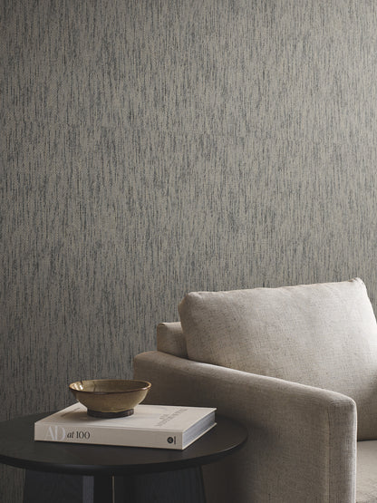 Beige fabric sofa with cushion beside a round black side table holding a beige bowl and stacked books, grey textured wall.