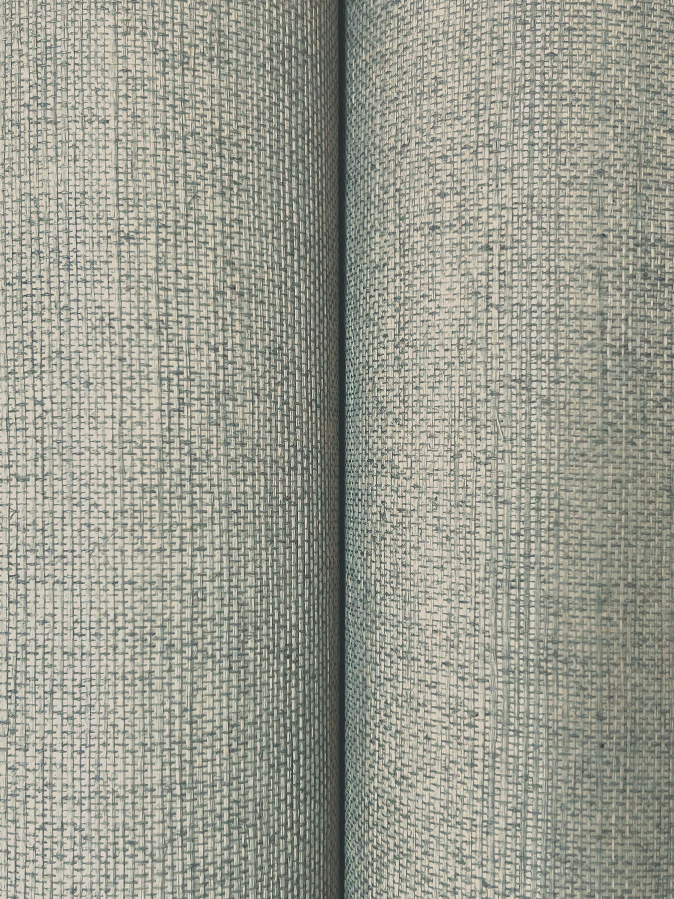 Close-up of light blue-gray sisal wallpaper with a fine woven grid texture; two rolls side by side.