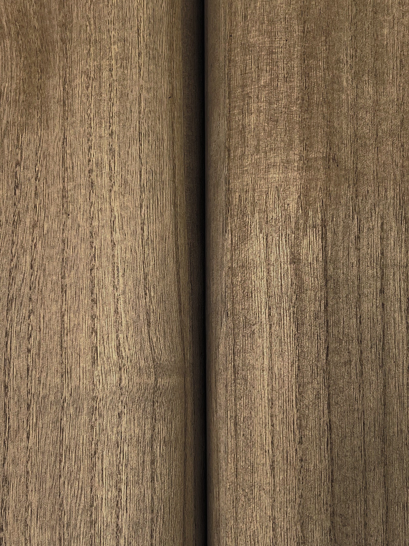Close-up of brown wood veneer with vertical grain, seam between two panels, warm oak-like finish.