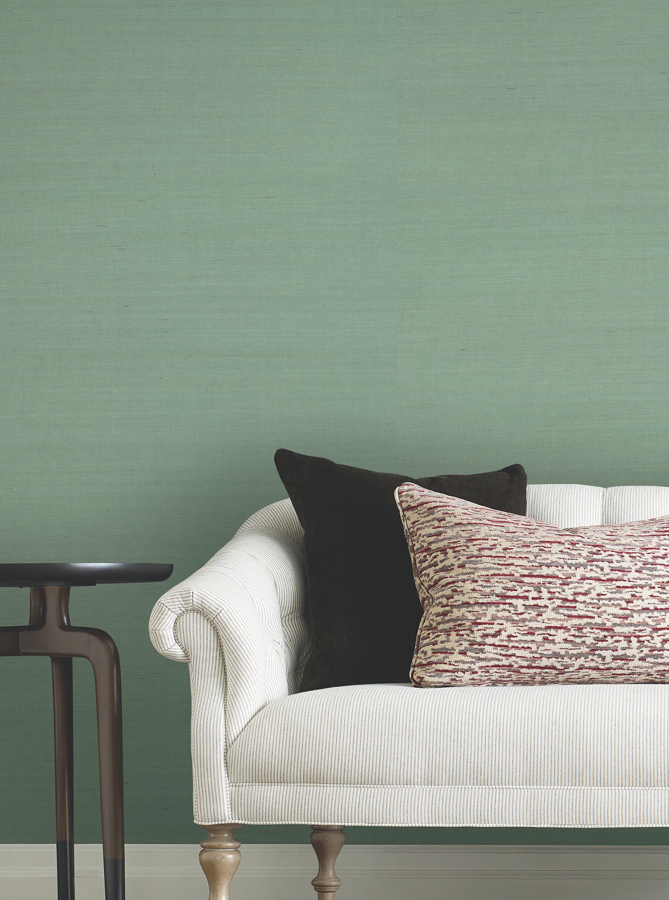 Cream fabric sofa with rolled arms, black and patterned red cushions, dark wood side table, green wall backdrop.