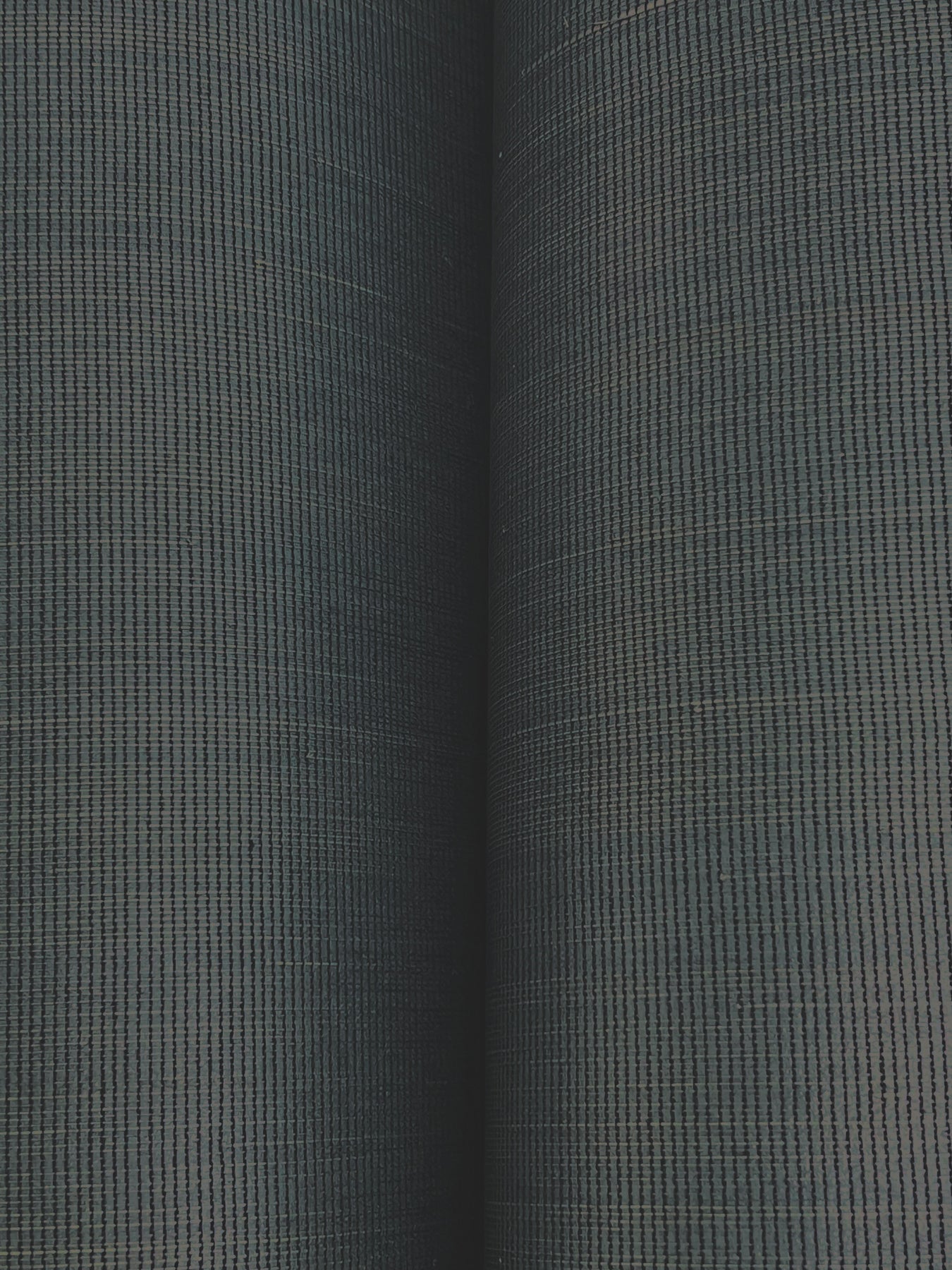 Close-up of dark grey-green wallpaper with a tight grid pattern; two rolled wallpaper edges visible.