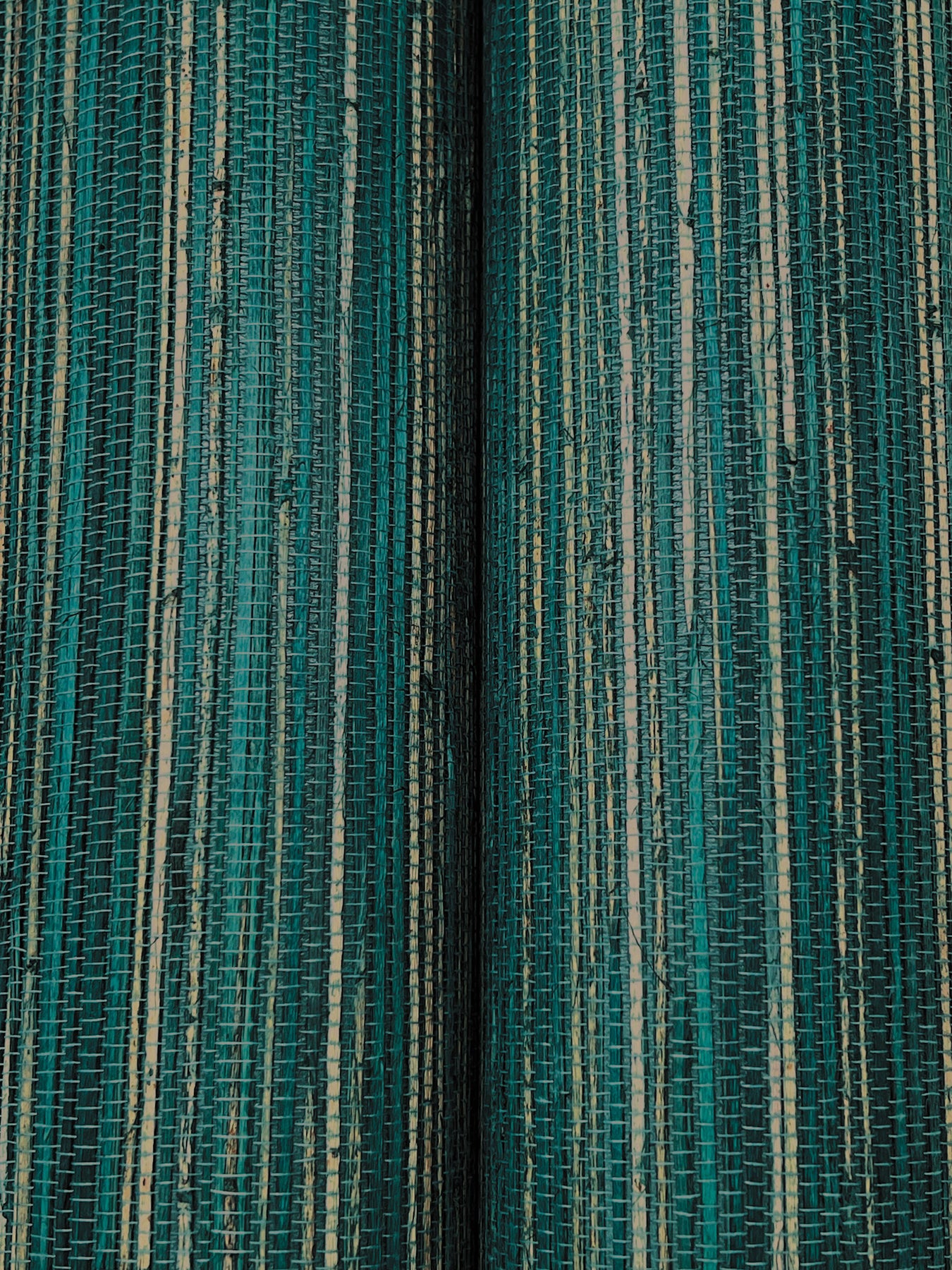 Close-up of teal and turquoise hemp grasscloth wallpaper with thin cream lines; two panels with a dark seam between them.