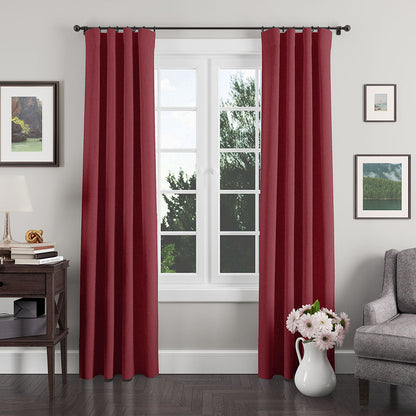 Deep red curtains on a black rod framing a window in a cozy living room with a gray sofa and white vase of pink flowers.