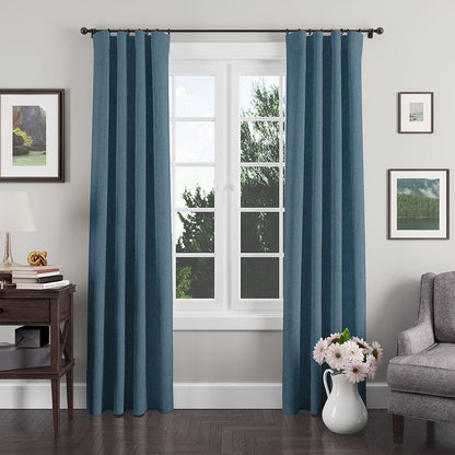 Blue textured floor-length curtains with metal grommets on a black rod framing a white-paneled window in a cozy living room.