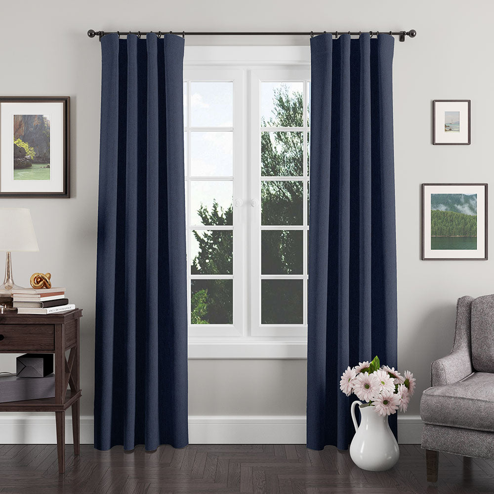 Navy blue grommet-top curtains frame a bright window in a cozy living room with lamp & vase of flowers.