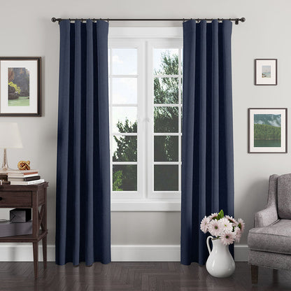 Navy blue grommet-top curtains frame a bright window in a cozy living room with lamp & vase of flowers.