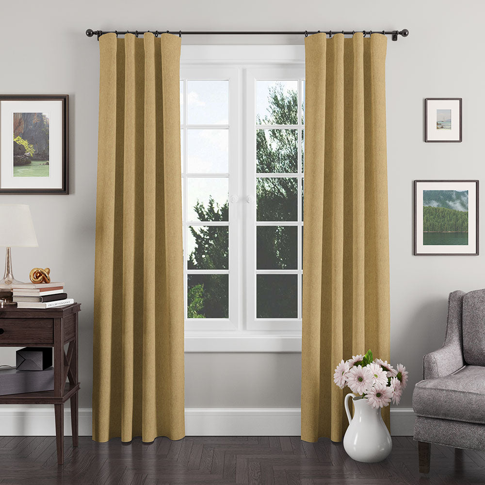 Golden-beige textured curtains on a black rod frame a white-paneled window in a cozy living room with sofa and vase of pink flowers.