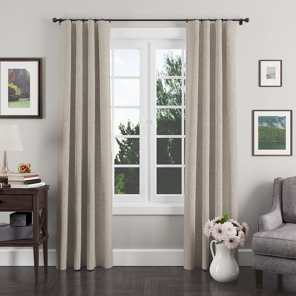 Beige textured floor-length curtains frame a sunlit window in a gray living room with a dark wood side table and framed art.