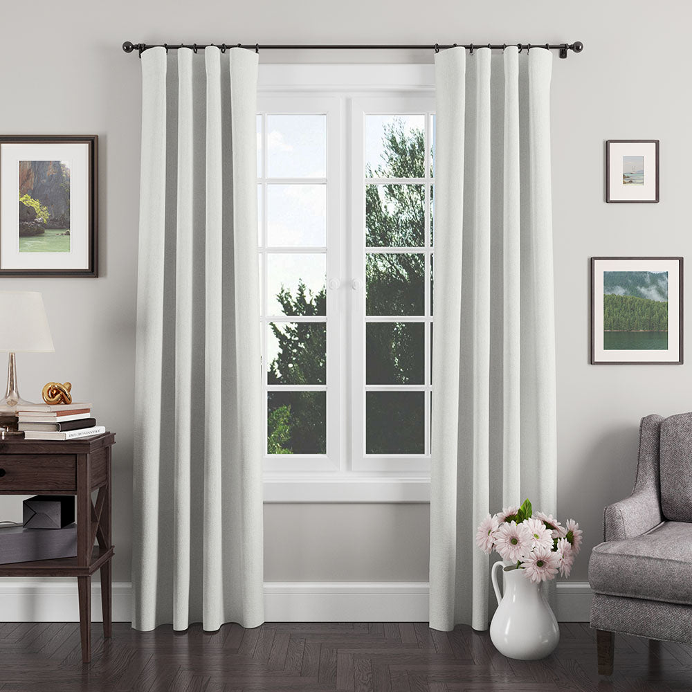 Light gray textured curtains on a dark rod frame a white-paned window in a living room with wooden console and pink flowers.