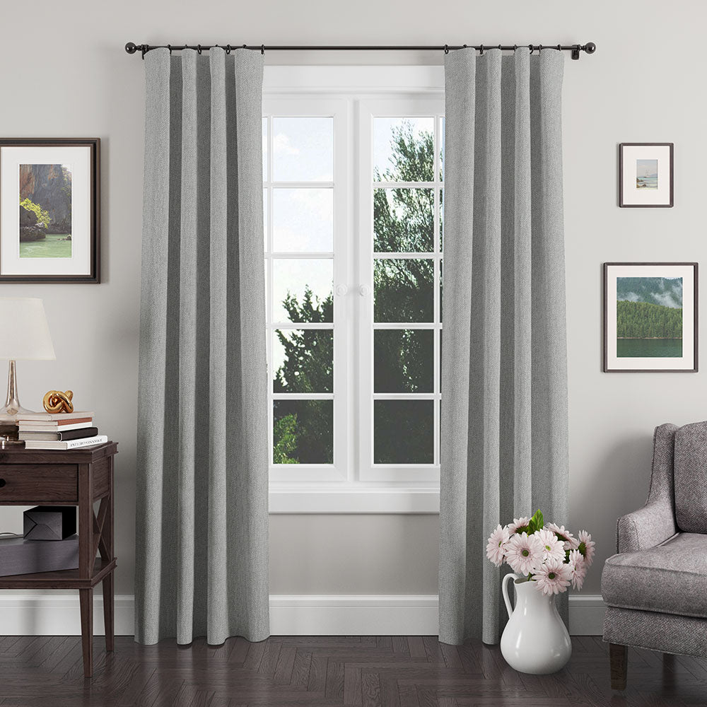 Grey textured floor-length curtains on a black rod, framing a white-framed window in a modern living room.