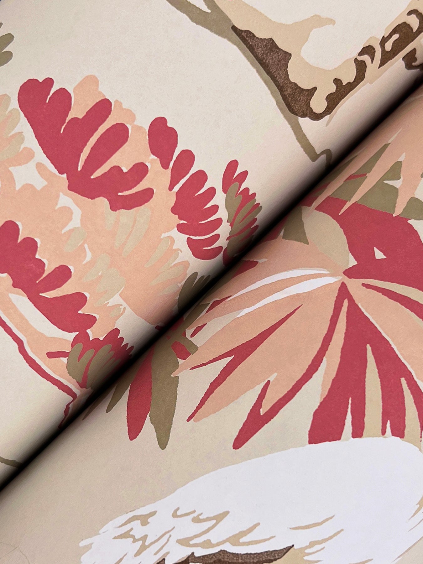 Close-up of a folded beige wallpaper swatch with a large pink, coral and peach floral pattern and brown accents.