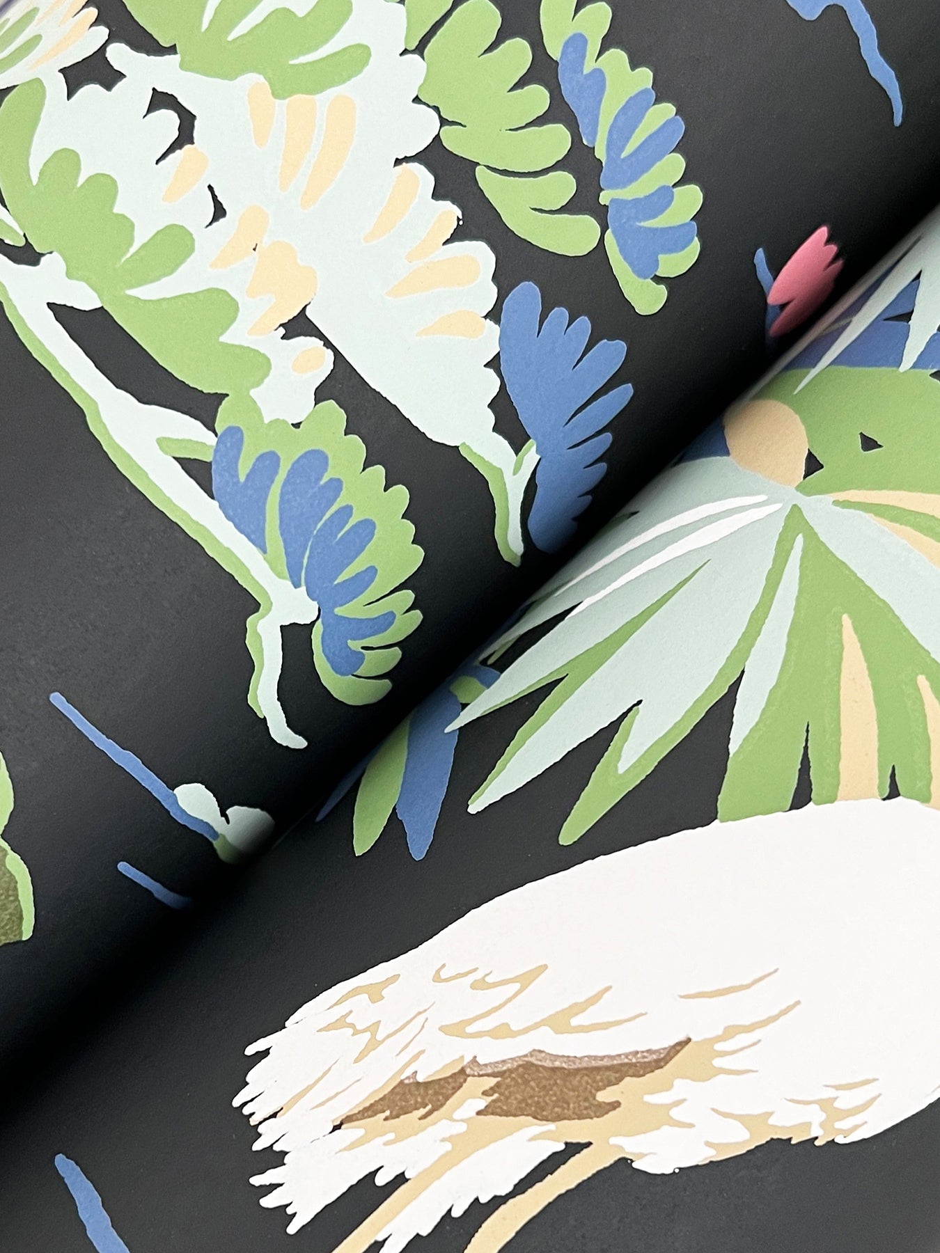 Close-up of bold tropical leaf print on dark wallpaper; lime green, pale yellow, blue, and beige leaves.