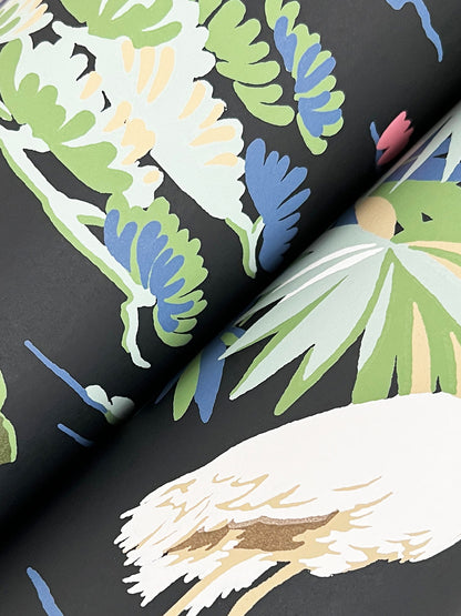 Close-up of bold tropical leaf print on dark wallpaper; lime green, pale yellow, blue, and beige leaves.