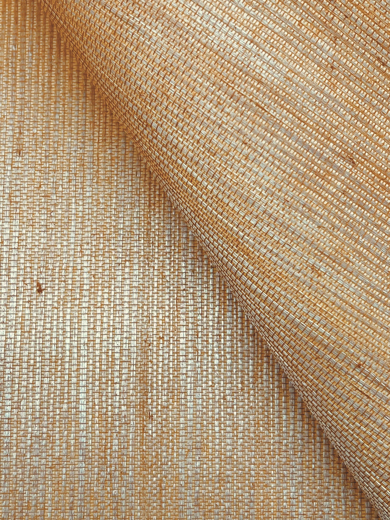 Beige and gold grasscloth wallpaper close-up with a woven texture and metallic threads, featuring a rolled corner.