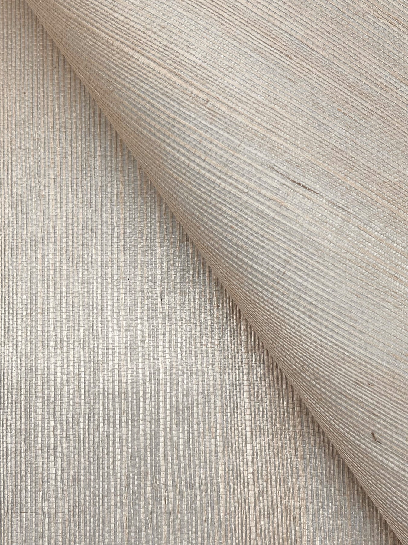 Beige grasscloth wallpaper with a linen-like woven texture and visible vertical ribs, shown with a folded corner.